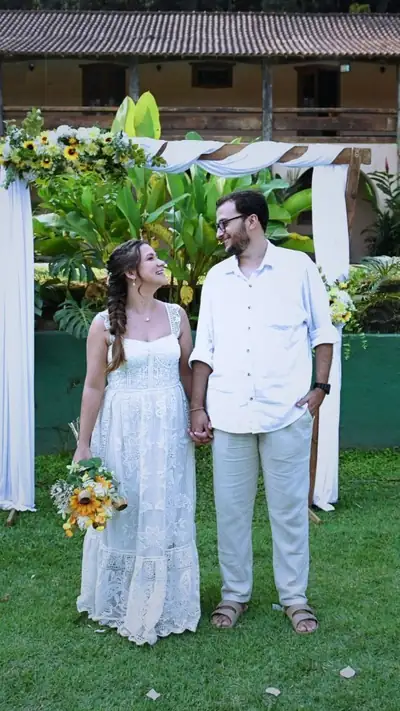 Casal de noivos de mãos dadas diante do arco de flores